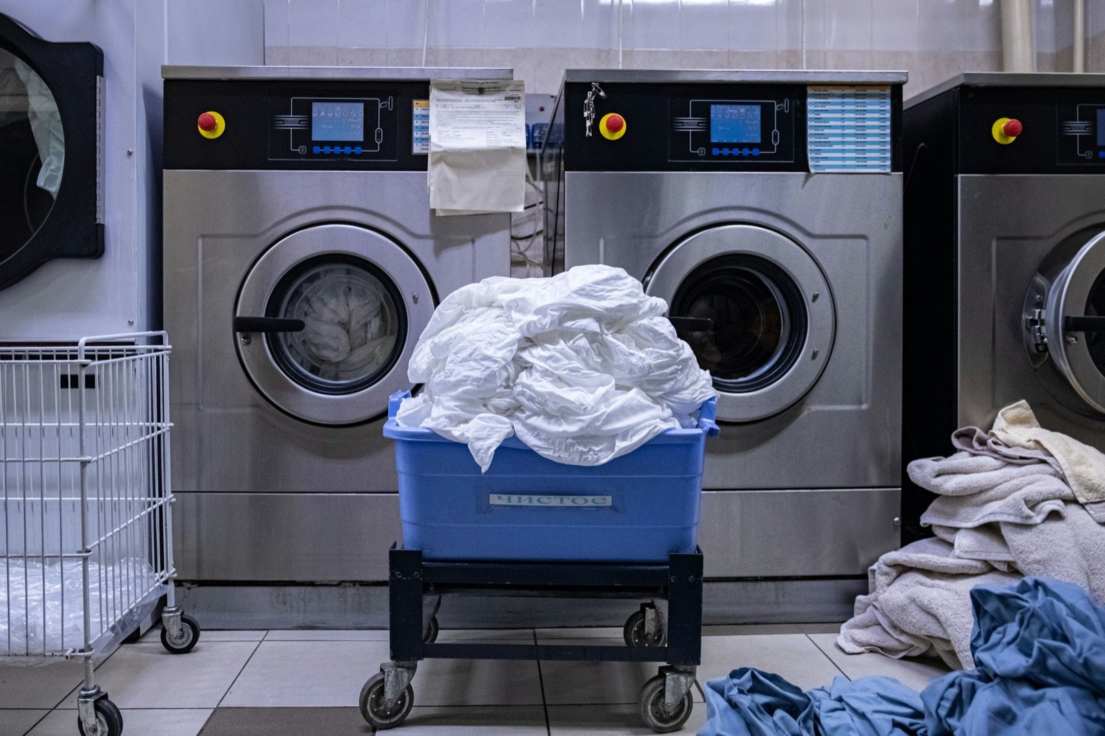 Mixed laundry in a blue basket in front of washing machines
