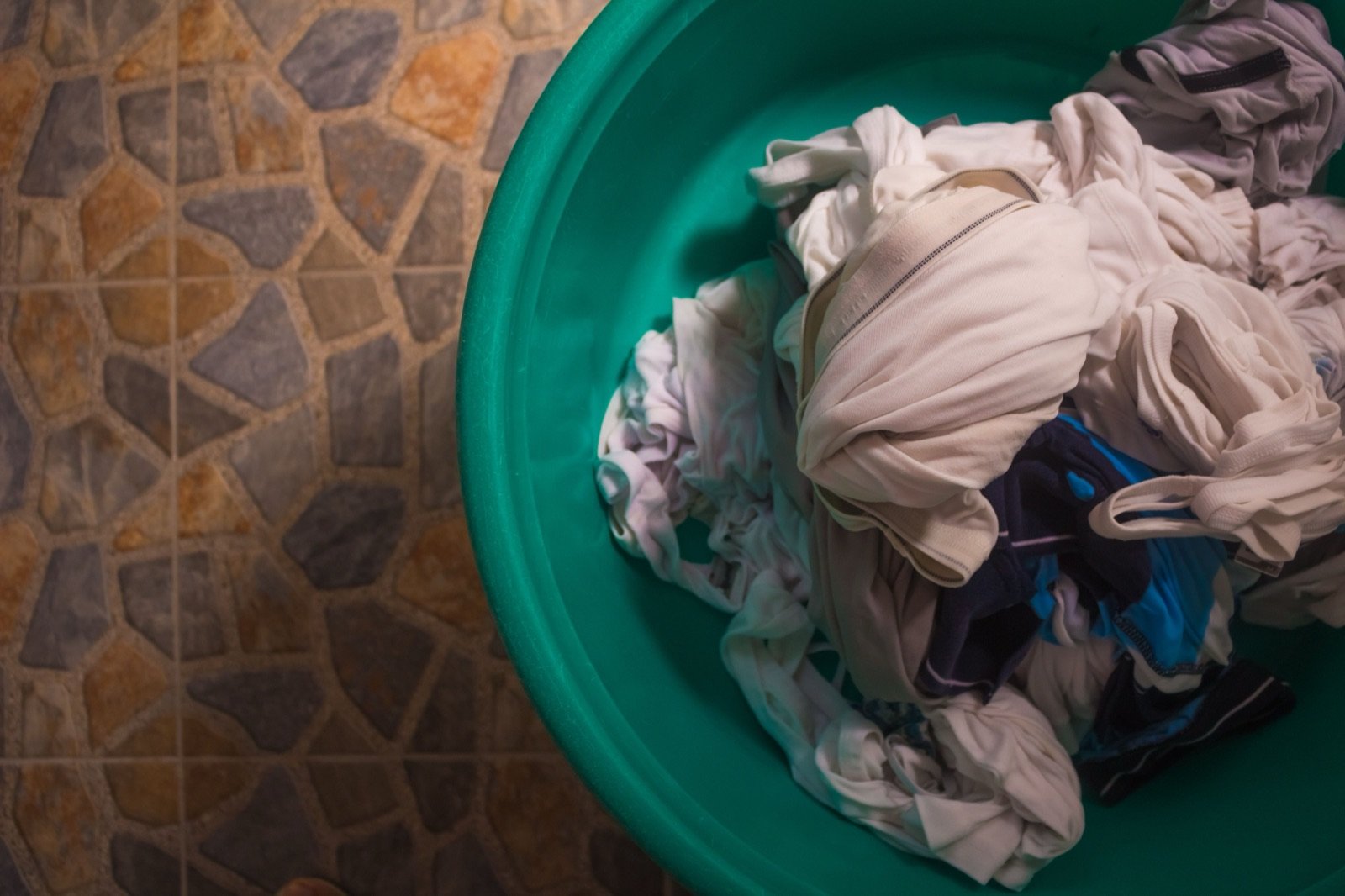 Crumpled clothes in a laundry basket on a tiled floor